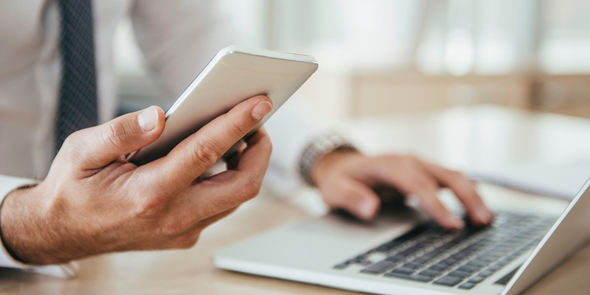 Image of person holding a smart phone and typing on laptop