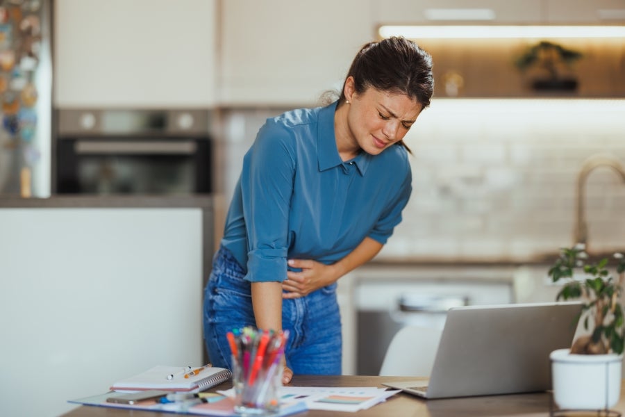 Woman doubled over in pain while working at her desk