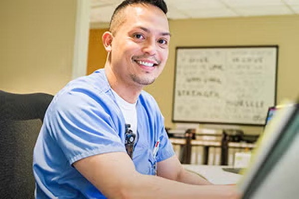 Male nurse smiling while working on computer at office