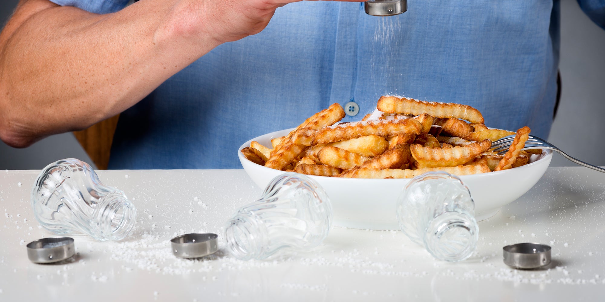 Person dumping salt on french fries with empty salt shakers around