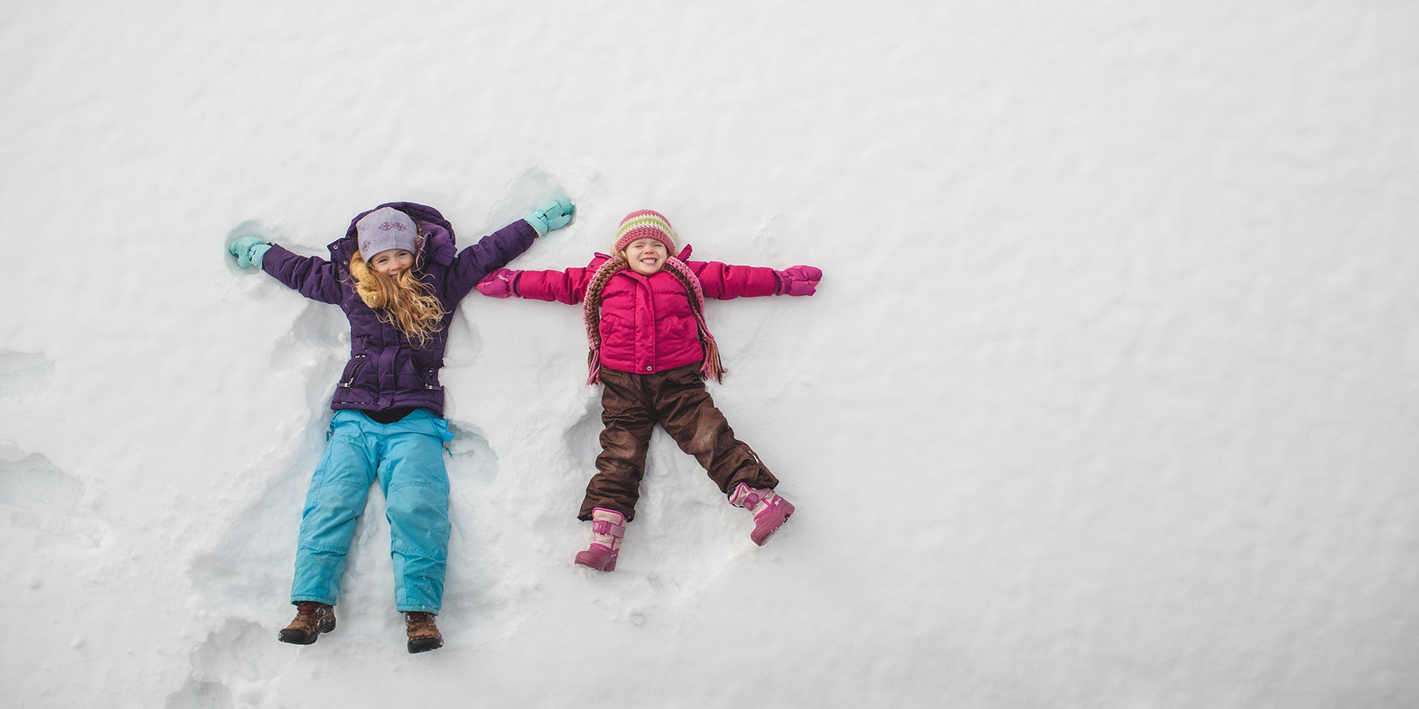 Two children making snow angels outside in snow